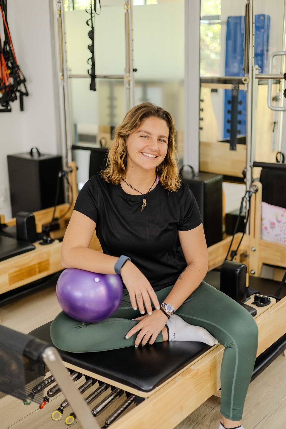Pilates instructor Myrren sitting on a reformer with a small Pilates ball at Pilates Dynamics