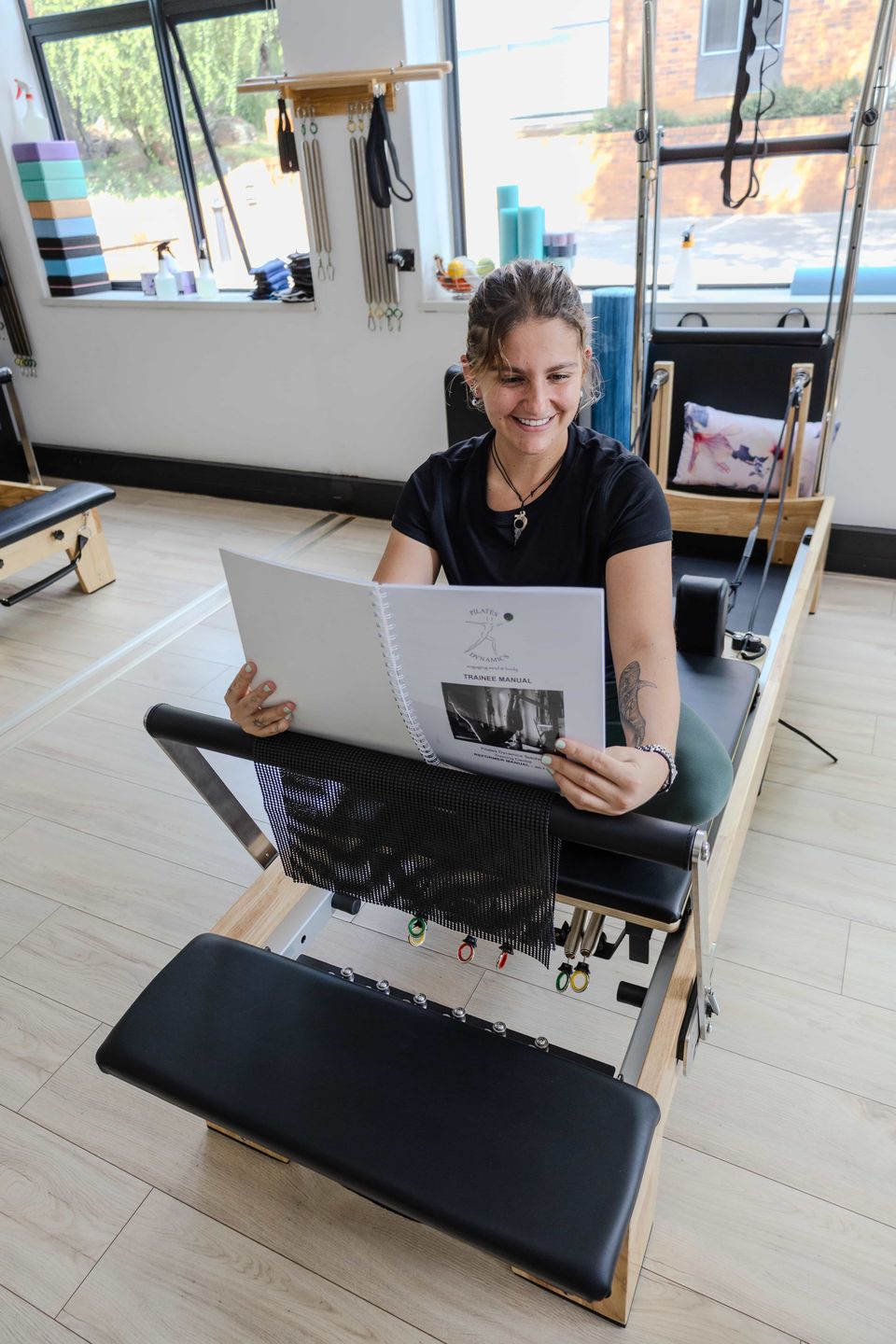 A Pilates teacher training student reading the Pilates Dynamics trainee manual on a reformer in the Randburg studio