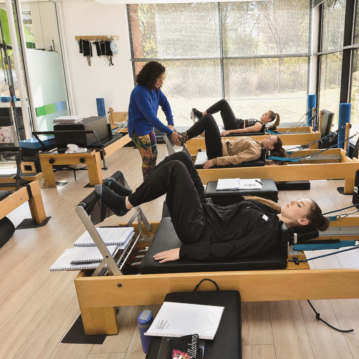 A row of reformers in the studio, an instructor guiding a client's footwork